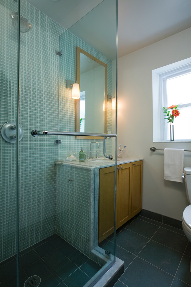 Photo of a modern ensuite bathroom in New York with a submerged sink, recessed-panel cabinets, medium wood cabinets, marble worktops, a corner shower, a two-piece toilet, green tiles, glass tiles, white walls and ceramic flooring.