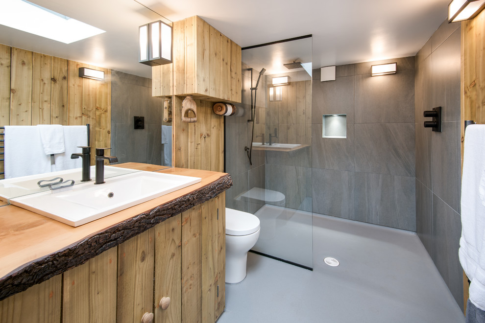 Diseño de cuarto de baño bohemio pequeño con puertas de armario de madera oscura, ducha abierta, sanitario de una pieza, paredes grises, suelo de linóleo, aseo y ducha, lavabo encastrado y encimera de madera