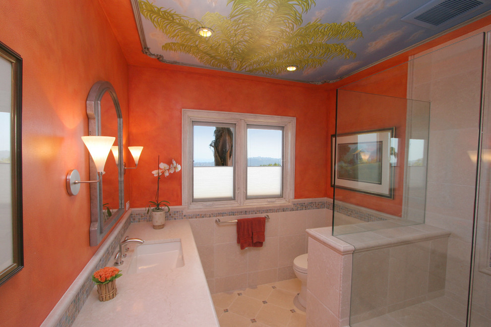 Immagine di una stanza da bagno mediterranea di medie dimensioni con lavabo sottopiano, ante in stile shaker, doccia ad angolo, WC a due pezzi, ante bianche, top in pietra calcarea, piastrelle multicolore, pareti arancioni e pavimento in pietra calcarea