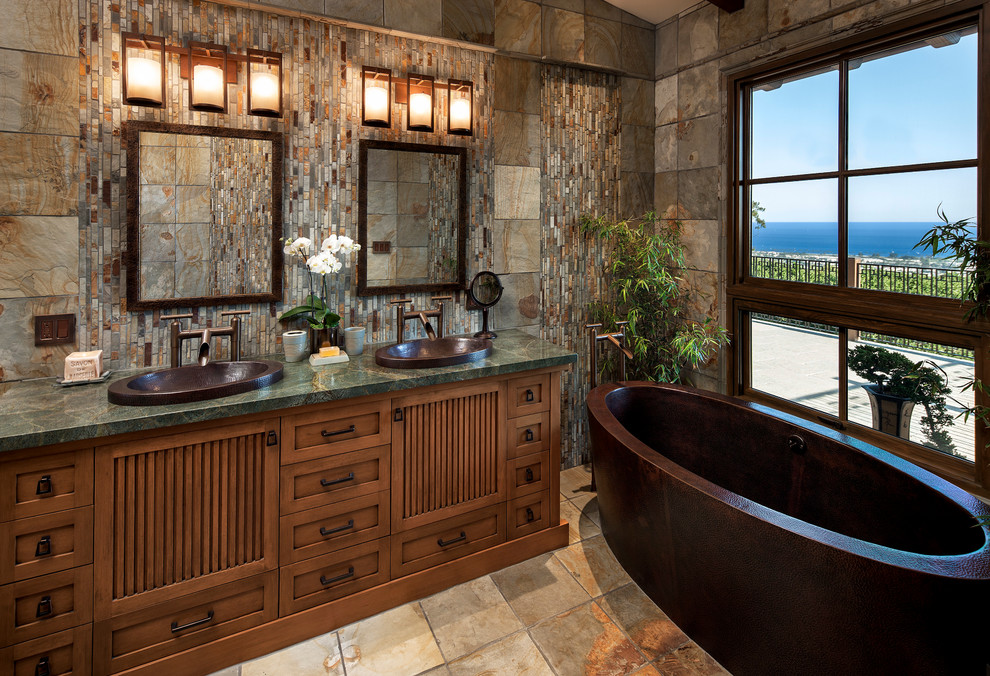 Mid-sized master stone tile, brown tile and gray tile slate floor freestanding bathtub photo in Santa Barbara with a drop-in sink, furniture-like cabinets, medium tone wood cabinets, granite countertops, a two-piece toilet and multicolored walls