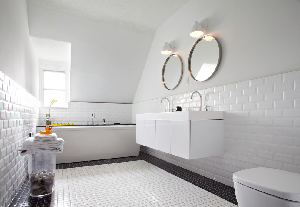 Cette image montre une salle de bain design avec un placard à porte plane, des portes de placard blanches, une baignoire indépendante, un carrelage blanc, un mur blanc et du carrelage bicolore.