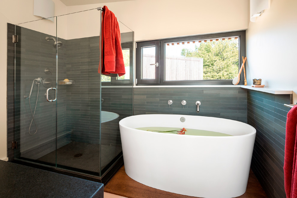 Foto på ett mellanstort minimalistiskt en-suite badrum, med ett fristående badkar, en hörndusch, grå kakel, skifferkakel, vita väggar, mellanmörkt trägolv, bänkskiva i täljsten, brunt golv och dusch med gångjärnsdörr