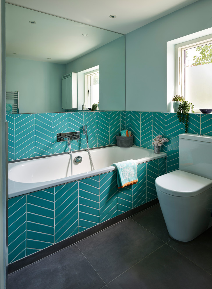 Modernes Badezimmer mit Einbaubadewanne, Toilette mit Aufsatzspülkasten, blauen Fliesen, blauer Wandfarbe und grauem Boden in London