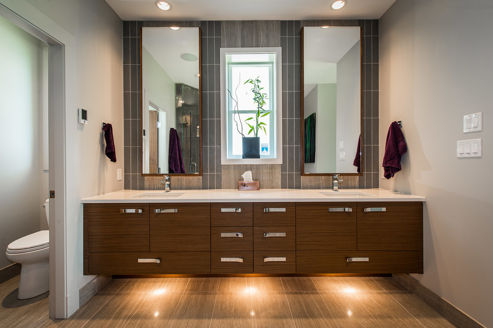 Cette image montre une salle de bain design en bois foncé avec un lavabo encastré, un placard à porte plane, un carrelage gris, un mur blanc et un sol en carrelage de céramique.