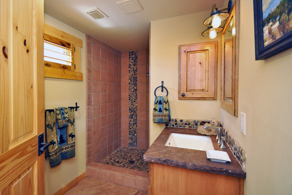 Foto på ett mellanstort amerikanskt badrum med dusch, med luckor med upphöjd panel, skåp i ljust trä, en dusch i en alkov, kakel i småsten, beige väggar, klinkergolv i terrakotta, ett undermonterad handfat och bänkskiva i täljsten