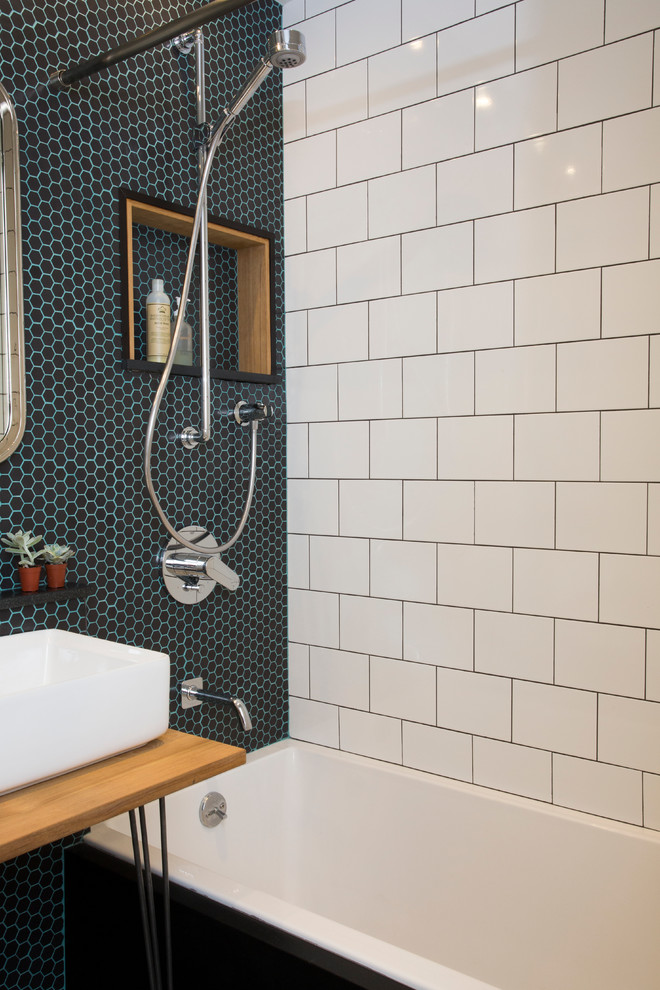 Inspiration for a small traditional ensuite bathroom in New York with a built-in bath, a wall mounted toilet, black tiles, glass tiles, black walls, mosaic tile flooring and a vessel sink.