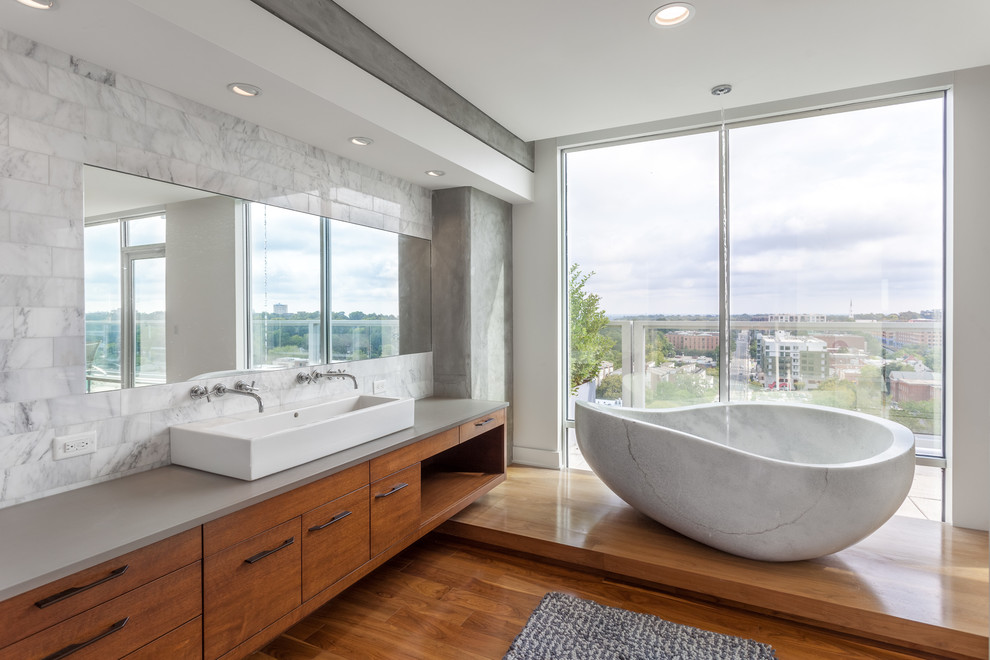 На фото: ванная комната в современном стиле с плоскими фасадами, фасадами цвета дерева среднего тона, отдельно стоящей ванной, белыми стенами, паркетным полом среднего тона и раковиной с несколькими смесителями