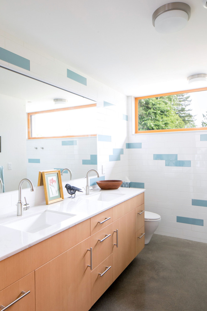 Immagine di una stanza da bagno moderna con ante lisce, ante in legno chiaro, piastrelle blu, piastrelle bianche, pavimento in cemento, lavabo sottopiano, pavimento grigio e top bianco