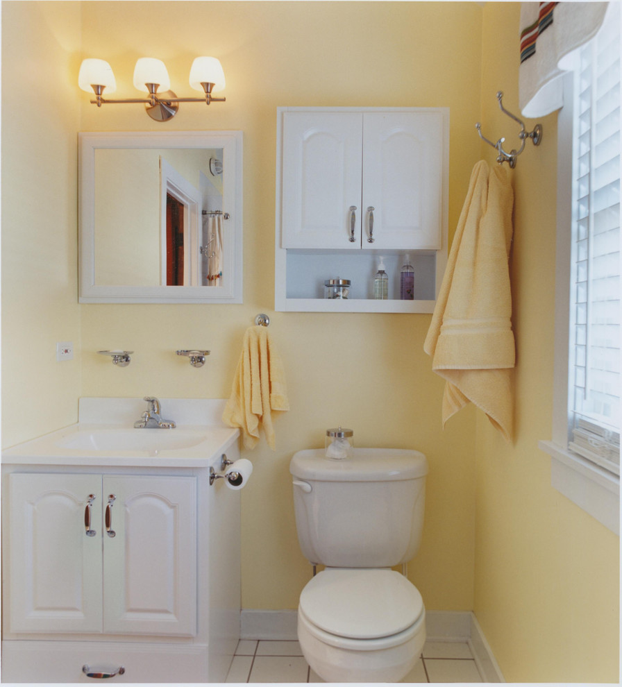 Inredning av ett maritimt litet badrum, med ett integrerad handfat, luckor med upphöjd panel, vita skåp, marmorbänkskiva, ett badkar i en alkov, en dusch/badkar-kombination, en toalettstol med separat cisternkåpa, vit kakel, keramikplattor, gula väggar och klinkergolv i keramik