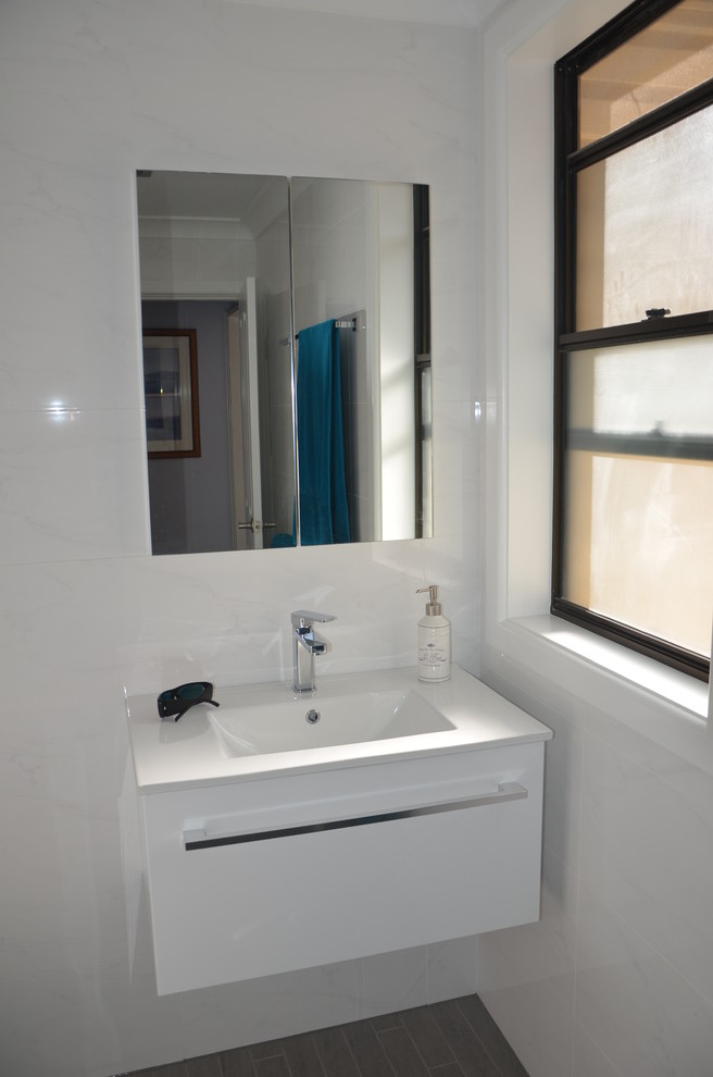 Foto di una stanza da bagno minimal con lavabo integrato, doccia aperta, WC monopezzo, ante lisce, ante bianche, top in superficie solida, piastrelle bianche e piastrelle in gres porcellanato