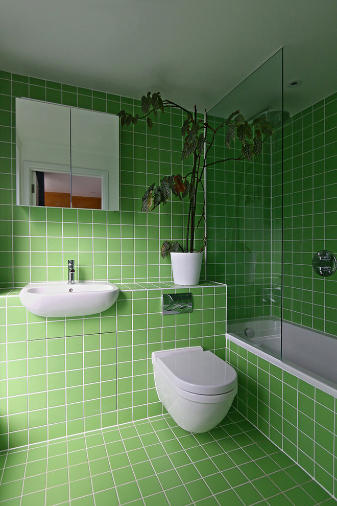 Idéer för att renovera ett mellanstort funkis grön grönt en-suite badrum, med gröna skåp, ett platsbyggt badkar, en dusch/badkar-kombination, en vägghängd toalettstol, grön kakel, keramikplattor, gröna väggar, klinkergolv i keramik, ett nedsänkt handfat, kaklad bänkskiva och grönt golv