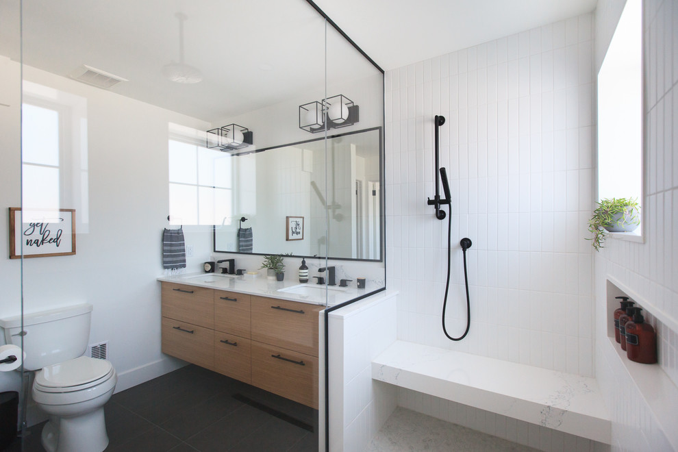 This is an example of a medium sized contemporary ensuite bathroom in Toronto with flat-panel cabinets, medium wood cabinets, an alcove shower, a one-piece toilet, white tiles, metro tiles, white walls, slate flooring, a submerged sink, quartz worktops, grey floors, a hinged door and white worktops.