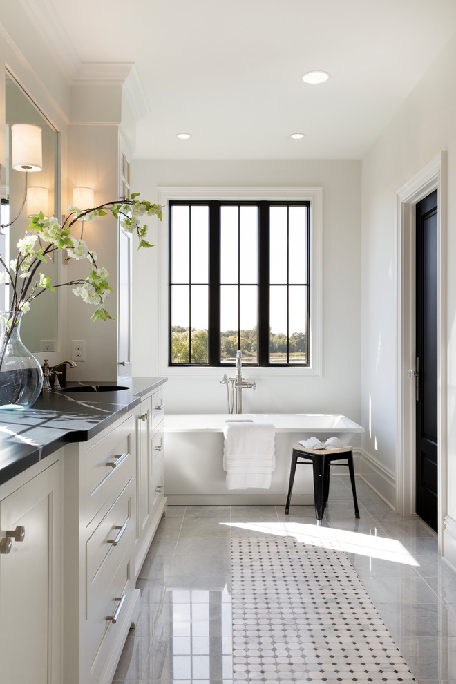 Expansive beach style ensuite bathroom in Minneapolis with white cabinets, a freestanding bath, a walk-in shower, ceramic flooring, a built-in sink, engineered stone worktops, grey floors and black worktops.
