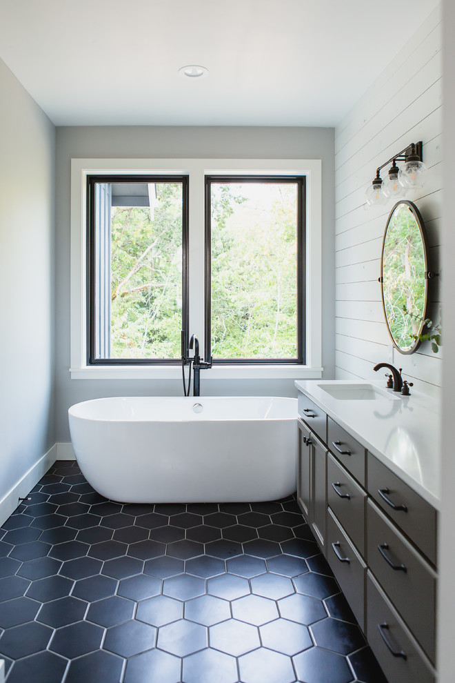 Diseño de cuarto de baño de estilo de casa de campo con armarios con paneles lisos, puertas de armario negras, bañera exenta, paredes grises, aseo y ducha, lavabo bajoencimera, suelo negro y encimeras blancas