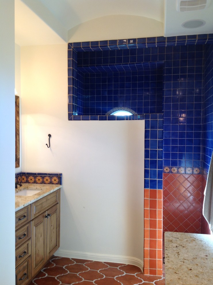 Photo of a large mediterranean bathroom in Austin with raised-panel cabinets, medium wood cabinets, granite worktops, a built-in shower, multi-coloured tiles, cement tiles, white walls and terracotta flooring.