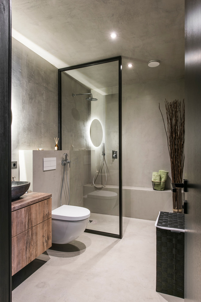 Exempel på ett mellanstort modernt brun brunt badrum med dusch, med släta luckor, en vägghängd toalettstol, grå väggar, betonggolv, träbänkskiva, grått golv, med dusch som är öppen, skåp i mellenmörkt trä, en öppen dusch och ett fristående handfat