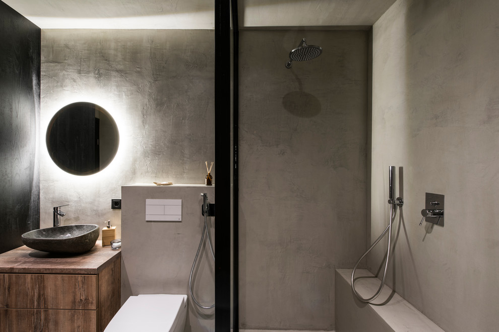Exemple d'une salle de bain tendance avec un placard à porte plane, des portes de placard marrons, un espace douche bain, WC suspendus, des carreaux de béton, un mur gris, sol en béton ciré, un lavabo suspendu, un plan de toilette en bois, un sol gris et aucune cabine.