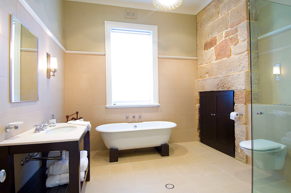 Diseño de cuarto de baño contemporáneo con lavabo bajoencimera, puertas de armario de madera en tonos medios, bañera exenta, ducha esquinera, sanitario de pared, baldosas y/o azulejos beige y piedra