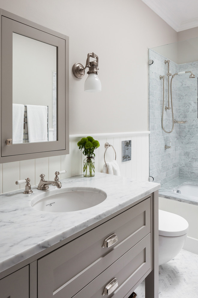 Klassisk inredning av ett stort en-suite badrum, med luckor med infälld panel, grå skåp, ett undermonterat badkar, en dusch/badkar-kombination, en vägghängd toalettstol, grå kakel, marmorkakel, grå väggar, marmorgolv, ett undermonterad handfat, marmorbänkskiva, grått golv och dusch med gångjärnsdörr