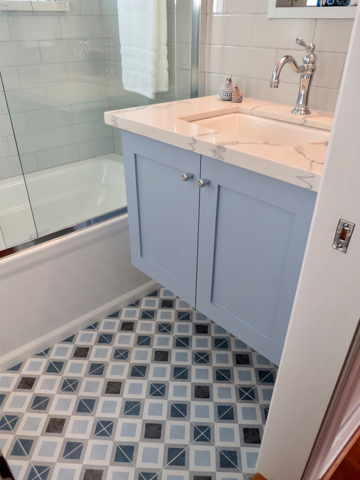 На фото: маленькая детская ванная комната в стиле неоклассика (современная классика) с фасадами в стиле шейкер, синими фасадами, ванной в нише, раздельным унитазом, серой плиткой, керамической плиткой, серыми стенами, полом из керамогранита, врезной раковиной, столешницей из искусственного кварца, синим полом, душем с раздвижными дверями, белой столешницей, тумбой под одну раковину и подвесной тумбой для на участке и в саду