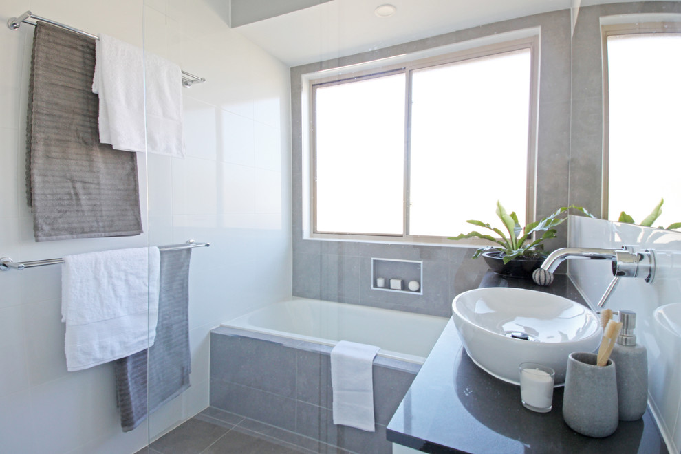 Photo of a small contemporary family bathroom in Brisbane with flat-panel cabinets, white cabinets, a built-in bath, a corner shower, a two-piece toilet, white tiles, ceramic tiles, white walls, terracotta flooring, a vessel sink, engineered stone worktops, grey floors, a hinged door and black worktops.