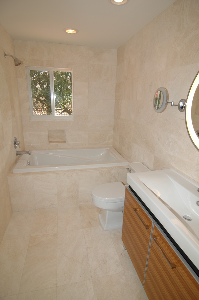 Example of a mid-sized trendy kids' travertine floor drop-in bathtub design in Miami with furniture-like cabinets and a one-piece toilet