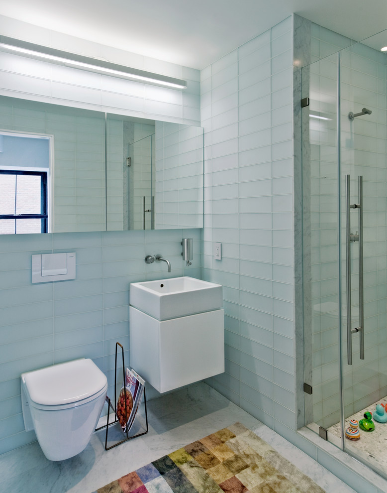 Inredning av ett modernt badrum, med en vägghängd toalettstol, glaskakel, ett väggmonterat handfat, en dusch i en alkov, vit kakel och vita skåp