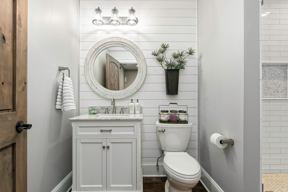 Inspiration for a farmhouse shower room bathroom in Columbus with recessed-panel cabinets, white cabinets, an alcove shower, a two-piece toilet, white tiles, metro tiles, grey walls, medium hardwood flooring, a submerged sink, marble worktops, brown floors and a hinged door.