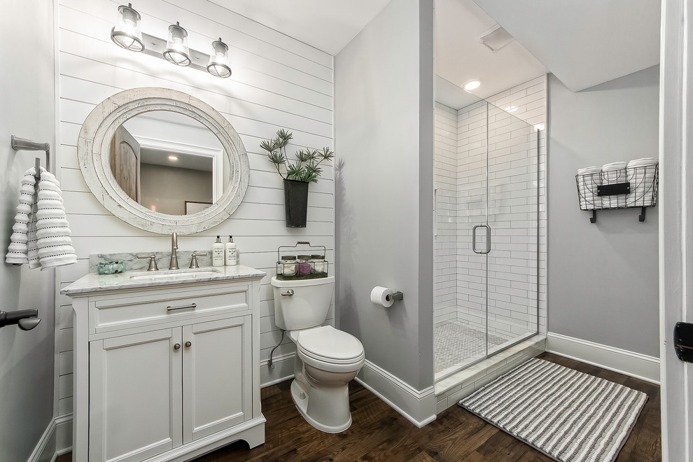 Пример оригинального дизайна: ванная комната среднего размера в стиле кантри с фасадами с утопленной филенкой, белыми фасадами, душем в нише, раздельным унитазом, белой плиткой, плиткой кабанчик, серыми стенами, паркетным полом среднего тона, душевой кабиной, врезной раковиной, мраморной столешницей, коричневым полом и душем с распашными дверями