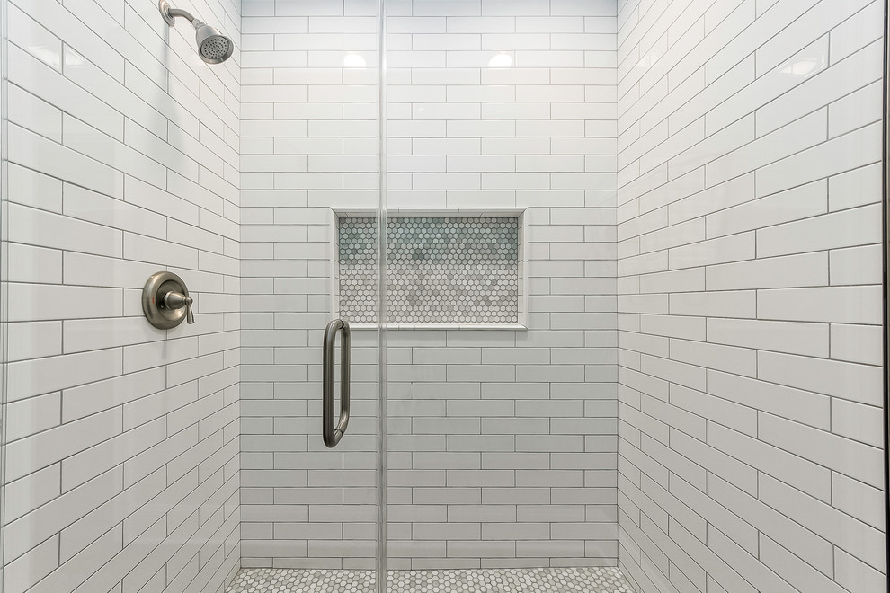 Inredning av ett lantligt badrum med dusch, med luckor med infälld panel, vita skåp, en dusch i en alkov, en toalettstol med separat cisternkåpa, vit kakel, tunnelbanekakel, grå väggar, mellanmörkt trägolv, ett undermonterad handfat, marmorbänkskiva, brunt golv och dusch med gångjärnsdörr
