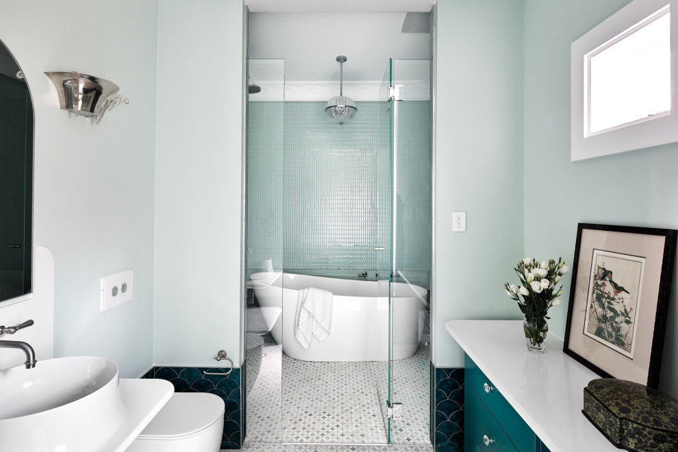 На фото: главная ванная комната в стиле неоклассика (современная классика) с плоскими фасадами, бирюзовыми фасадами, отдельно стоящей ванной, душевой комнатой, унитазом-моноблоком, синими стенами, настольной раковиной, разноцветным полом, душем с распашными дверями, белой столешницей, тумбой под одну раковину и встроенной тумбой с
