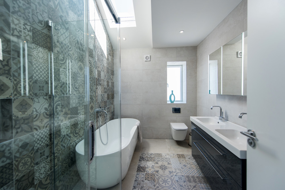 Photo of a medium sized contemporary ensuite bathroom in Dublin with black cabinets, flat-panel cabinets, a freestanding bath, a corner shower, a wall mounted toilet, brown tiles, grey tiles, grey walls, an integrated sink, multi-coloured floors and a hinged door.