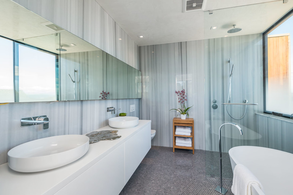Medium sized contemporary ensuite wet room bathroom in San Francisco with flat-panel cabinets, white cabinets, a freestanding bath, a wall mounted toilet, grey tiles, grey walls, a vessel sink, grey floors, an open shower, white worktops, mosaic tile flooring and solid surface worktops.