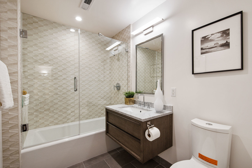 Bild på ett mellanstort funkis grå grått badrum, med möbel-liknande, bruna skåp, ett badkar i en alkov, en dusch/badkar-kombination, en toalettstol med hel cisternkåpa, beige kakel, keramikplattor, vita väggar, klinkergolv i keramik, ett konsol handfat, marmorbänkskiva, grått golv och dusch med gångjärnsdörr