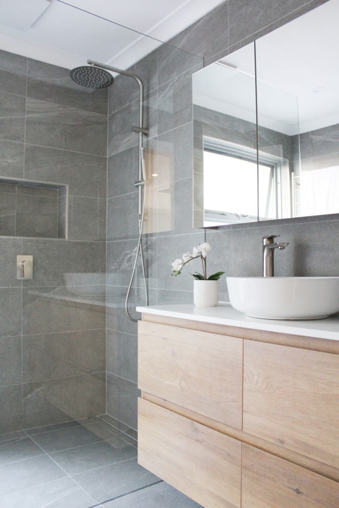 This is an example of a small modern ensuite bathroom in Perth with flat-panel cabinets, light wood cabinets, a walk-in shower, a two-piece toilet, grey tiles, porcelain tiles, grey walls, porcelain flooring, a vessel sink, engineered stone worktops, grey floors, an open shower, white worktops, a single sink and a floating vanity unit.