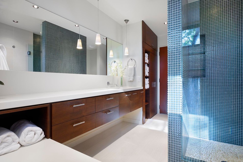 This is an example of a contemporary bathroom in Toronto with a submerged sink, flat-panel cabinets, dark wood cabinets, solid surface worktops, an alcove shower, blue tiles, glass tiles, white walls and porcelain flooring.