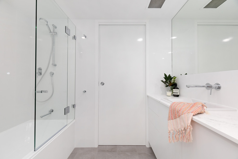 Inspiration for a small contemporary bathroom in Brisbane with white cabinets, a built-in bath, a shower/bath combination, a wall mounted toilet, white tiles, white walls, ceramic flooring, a built-in sink, grey floors, a hinged door, white worktops, a single sink and a built in vanity unit.