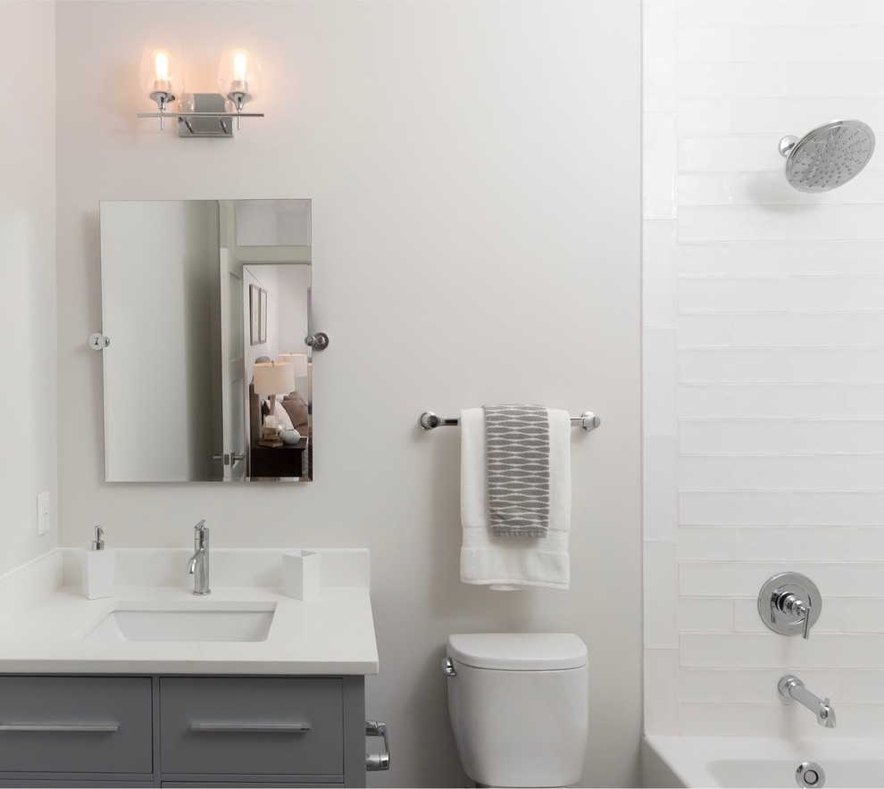 Réalisation d'une petite salle de bain design avec un placard à porte plane, des portes de placard grises, une baignoire posée, un combiné douche/baignoire, WC à poser, un carrelage blanc, des carreaux de céramique, un mur gris, un sol en carrelage de céramique, un lavabo encastré, un plan de toilette en quartz modifié et une cabine de douche avec un rideau.