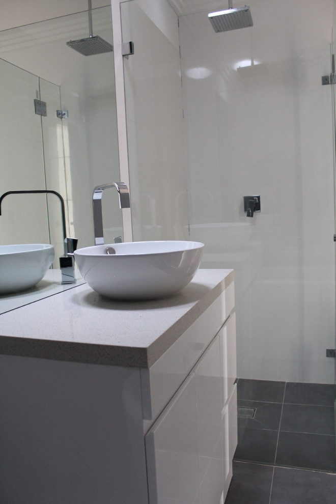 Bild på ett litet funkis badrum, med släta luckor, vita skåp, en hörndusch, vit kakel, vita väggar, ett fristående handfat, granitbänkskiva och dusch med gångjärnsdörr