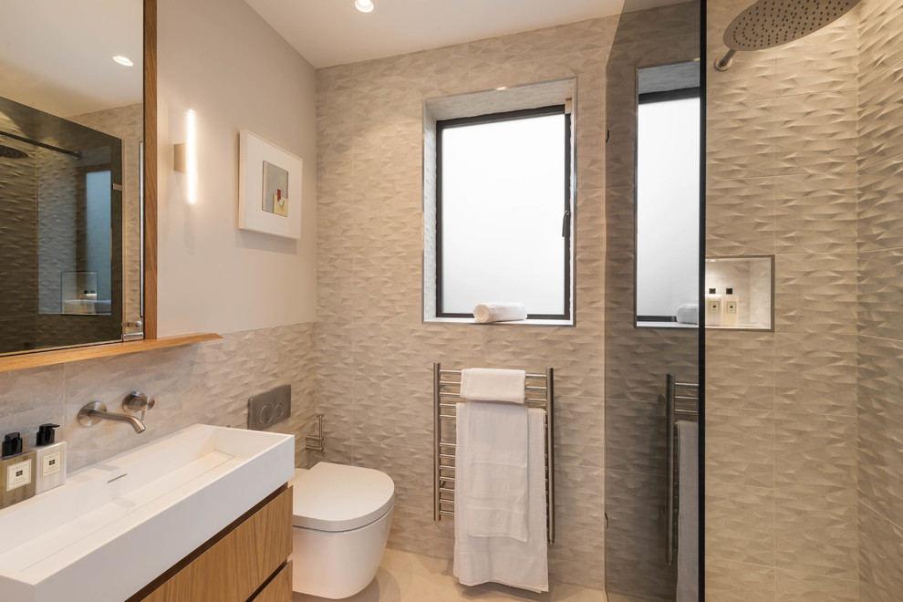 Medium sized contemporary bathroom in London with flat-panel cabinets, light wood cabinets, a walk-in shower, a wall mounted toilet, beige tiles, beige walls, a trough sink, beige floors and an open shower.