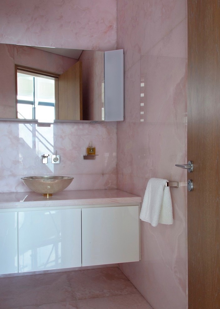 Cette image montre une petite salle de bain design pour enfant avec un placard à porte plane, des portes de placard blanches, une baignoire indépendante, une douche à l'italienne, WC à poser, un carrelage rose, des dalles de pierre, un mur rose, une vasque, un plan de toilette en onyx, un sol rose, une cabine de douche à porte coulissante et un plan de toilette rose.