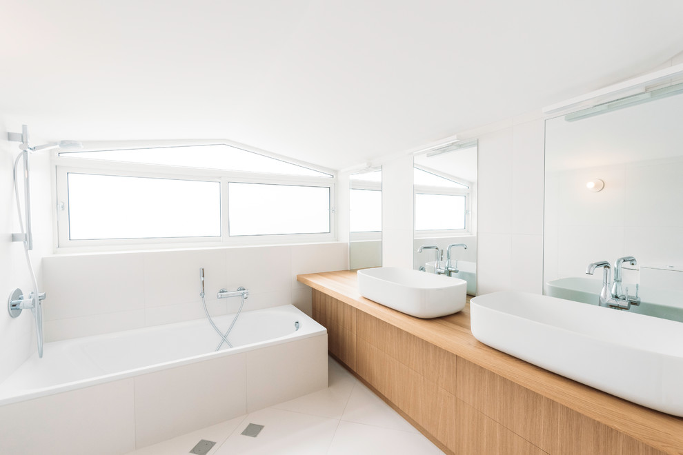 Exemple d'une salle de bain principale tendance en bois brun avec un placard à porte plane, une baignoire posée, un carrelage blanc, un mur blanc, une vasque, un plan de toilette en bois, un sol blanc et un plan de toilette marron.