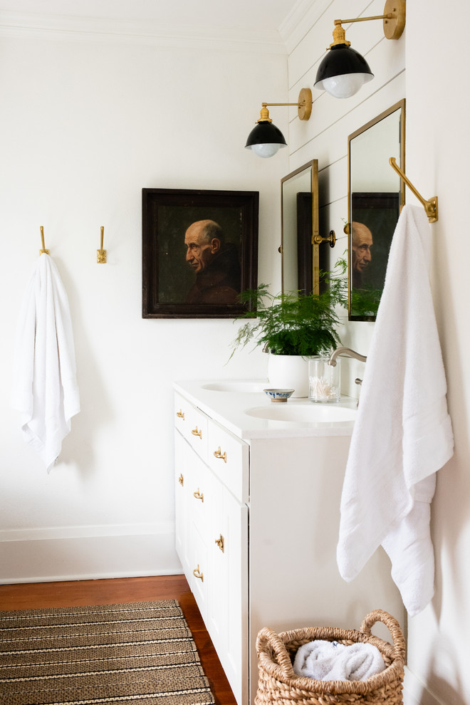 Immagine di una stanza da bagno tradizionale con ante bianche, pareti bianche, pavimento in legno massello medio, lavabo integrato, pavimento marrone e top bianco