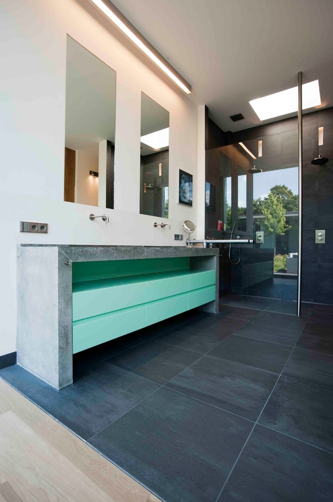 Example of a large trendy master gray tile ceramic tile bathroom design in New York with flat-panel cabinets, green cabinets, a wall-mount toilet, white walls, a trough sink and concrete countertops