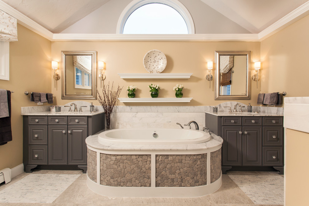 Immagine di una stanza da bagno padronale chic con ante con bugna sagomata, ante grigie, vasca da incasso, pareti gialle, lavabo sottopiano, pavimento beige e top grigio