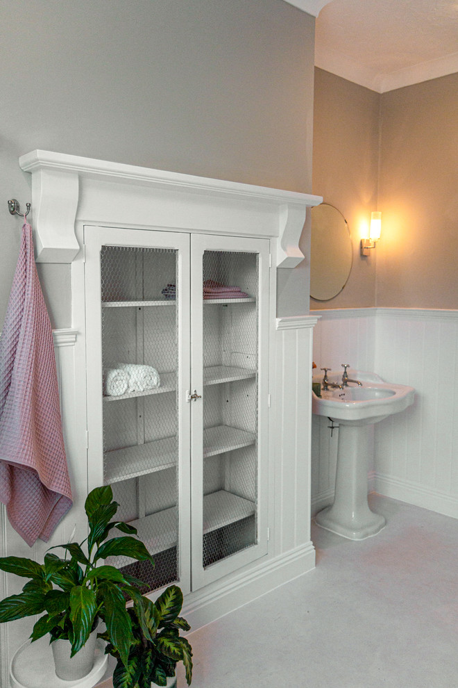 Klassisk inredning av ett stort badrum för barn, med ett badkar med tassar, en hörndusch, en toalettstol med hel cisternkåpa, grå väggar, linoleumgolv, ett piedestal handfat, vitt golv och dusch med skjutdörr