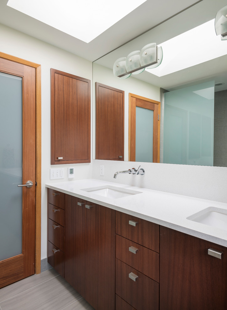 Idée de décoration pour une salle de bain design en bois foncé avec un lavabo encastré, un placard à porte plane et un plan de toilette blanc.