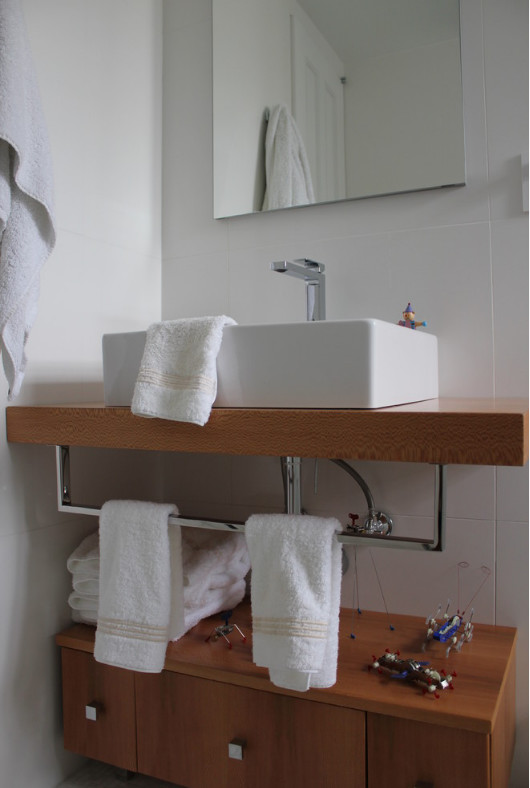 Imagen de cuarto de baño principal contemporáneo pequeño con puertas de armario de madera oscura, baldosas y/o azulejos blancos, paredes blancas, lavabo sobreencimera, encimera de madera y armarios con paneles lisos