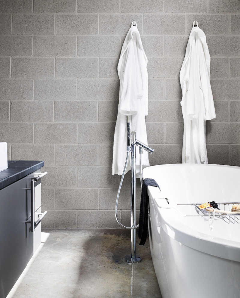 Diseño de cuarto de baño moderno con puertas de armario grises, bañera exenta y suelo de cemento
