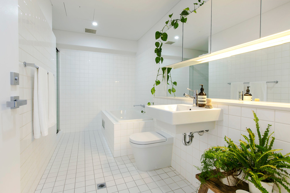 На фото: ванная комната среднего размера в современном стиле с угловой ванной, унитазом-моноблоком, белой плиткой, керамической плиткой, белыми стенами, полом из керамической плитки, душевой кабиной и подвесной раковиной с